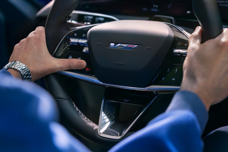 Close-up of a Man About to Press the V-Button on the 2026 OPTIQ-V Steering Wheel | Moses Cadillac of Charleston in Charleston WV